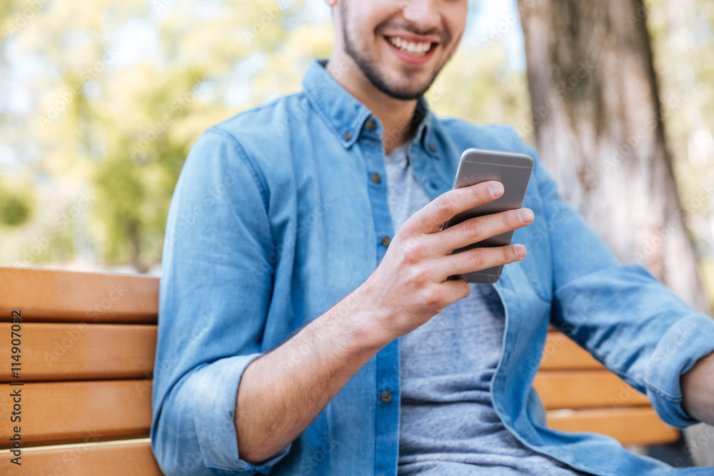 Cropped image of a smiling man with smartphone sitting outdoors Cropped image of a smiling man with smartphone sitting outdoors