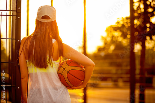 Frau mit einem Basketball schaut sich den Sonnenuntergang an photo