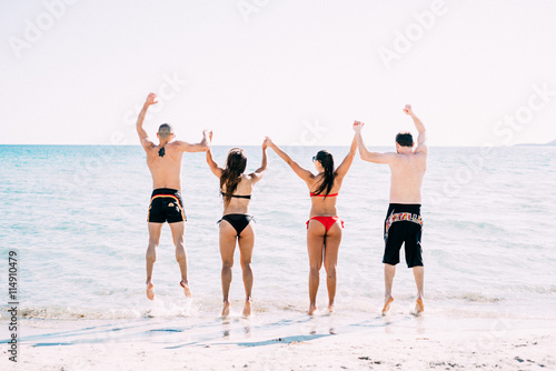 Back view of young multiethnic woman and man friends jumping hand in hand on the seashore - friendship, active, energy concept