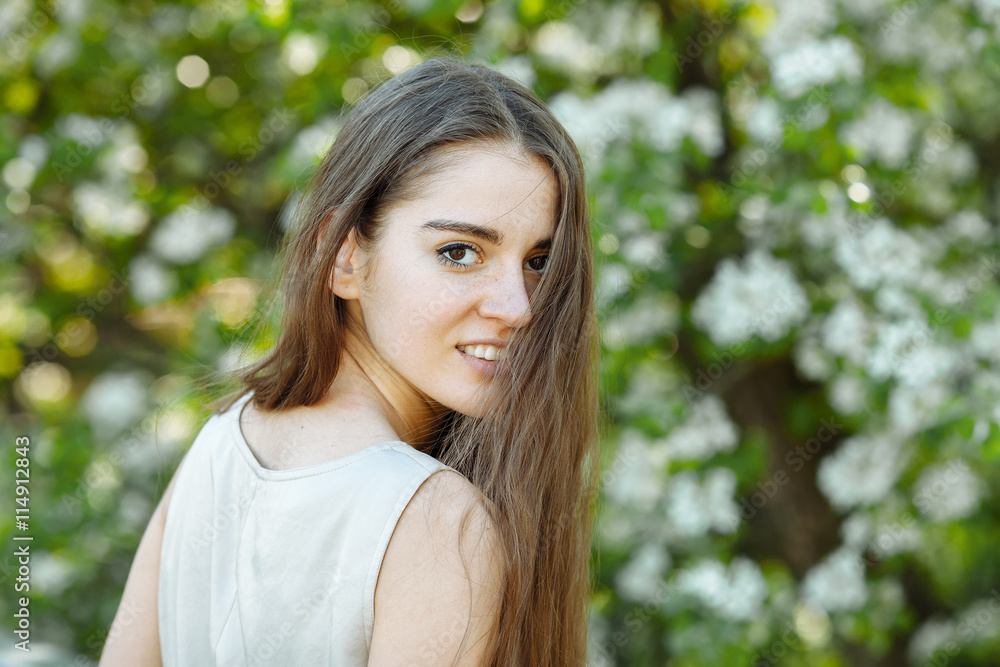 Portrait of the young beautiful brunette woman in pastel dress with extra long hair looks over her shoulder again blossoming tree outdoors