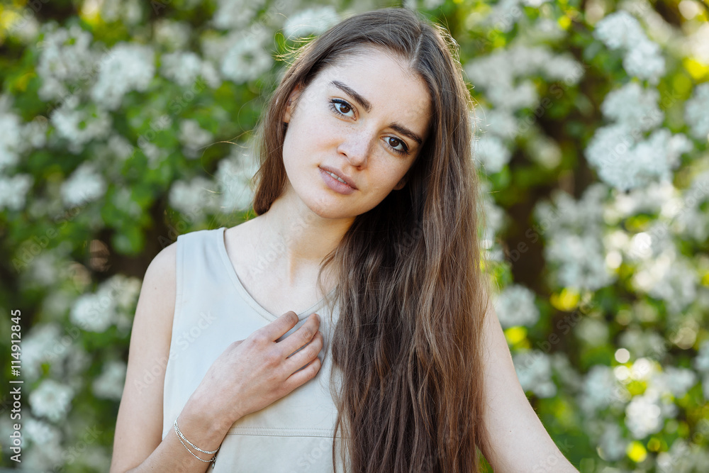 Portrait of the young beautiful brunette woman in pastel dress with extra long hair again blossoming tree outdoors Portrait of the young beautiful brunette woman in pastel dress with extra long hair again blossoming tree outdoors
