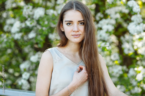 Portrait of the young beautiful brunette woman in pastel dress with extra long hair again blossoming tree outdoors