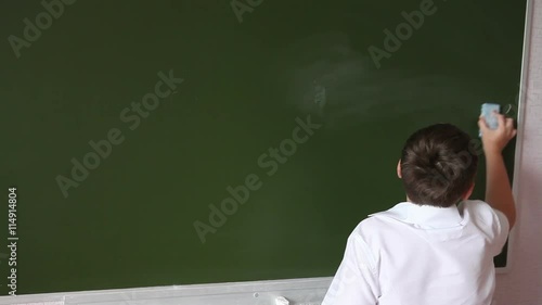 Teenager schoolboy wipes a blackboard to solve the example. photo