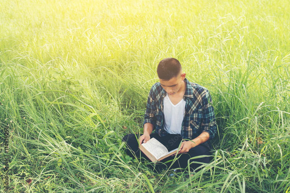 Young hipster man sitting on grassland reading book with nature Young hipster man sitting on grassland reading book with nature
