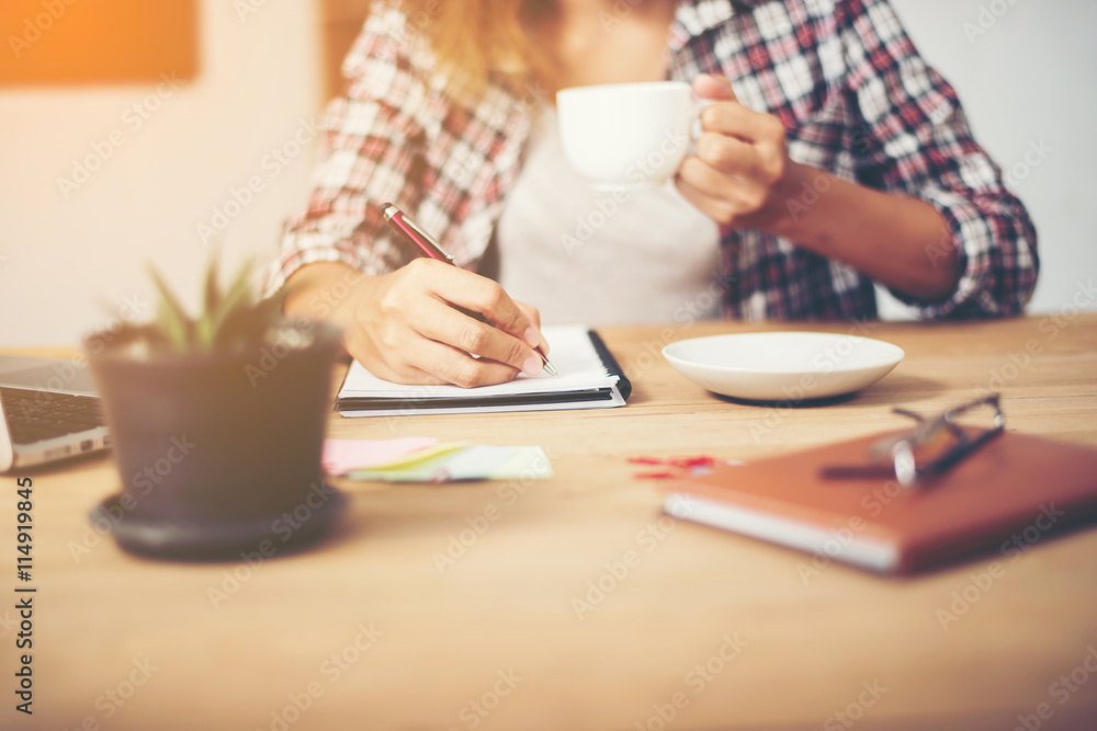 Business woman holding a cup of coffee and writing business plan Business woman holding a cup of coffee and writing business plan