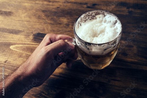 Quadro su tela Hand holding beer mug full of cold fresh alcohol drink