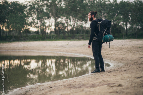 Bearded backpacker standing at lake