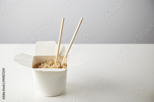 Tasty noodles with soy sause and spices inside blank takeaway paper box with chopsticks inside isolated on white