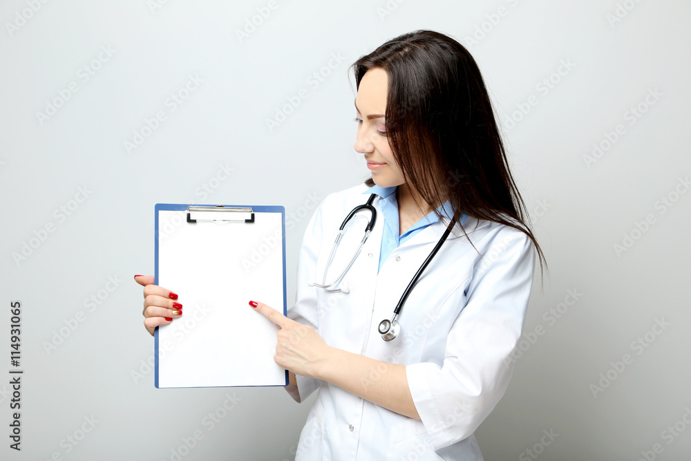Portrait of young medical doctor with clipboard on a grey backgr