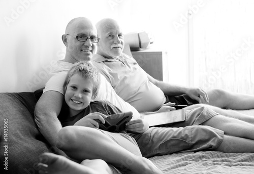 father, grandfather and son playing games on tablets and reading