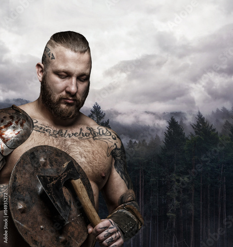 Brutal tattooed male viking with axe and shield.