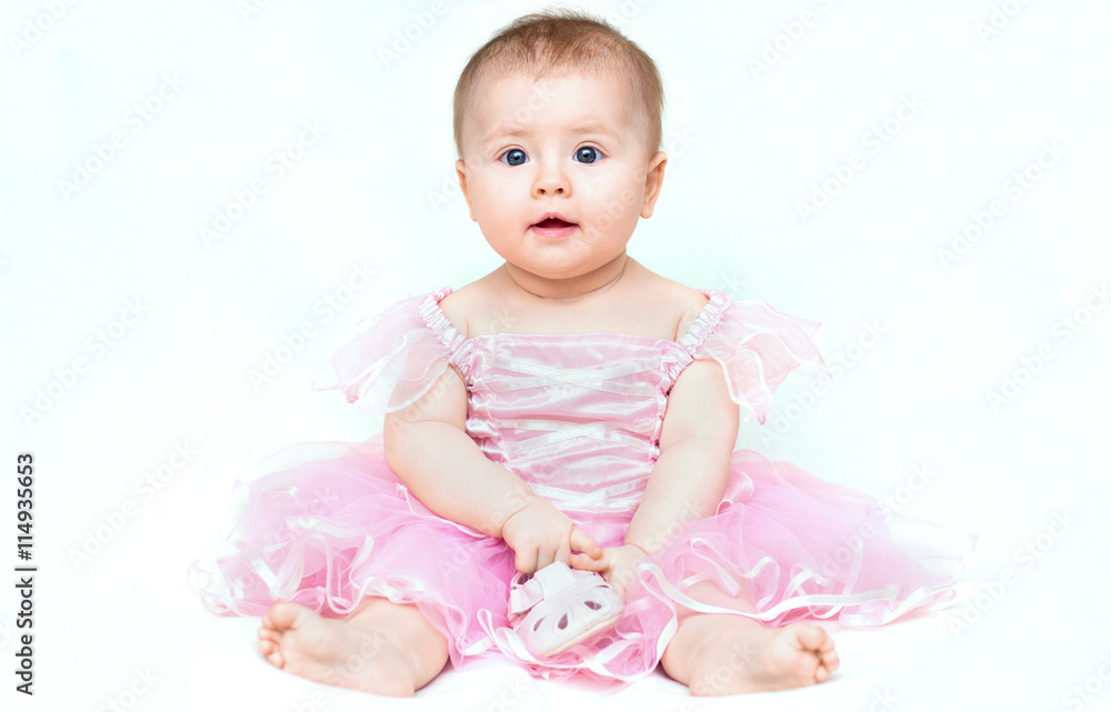 Adorable little baby girl in pink dress playing with her pink shoe.
