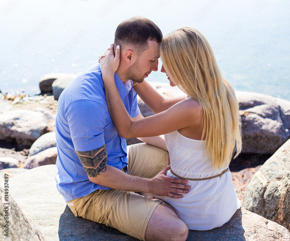 happy young beautiful couple sitting on rocky beach happy young beautiful couple sitting on rocky beach