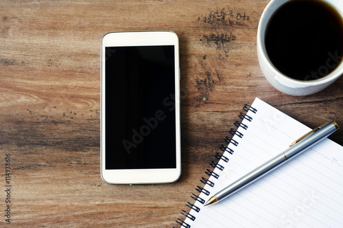 Business finance concept, blank notepad, smart phone, pen, coffee and calculator on a wooden table with copy space.