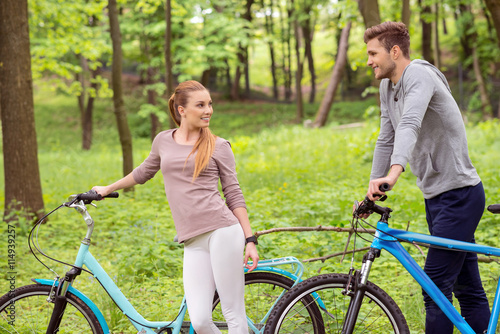 Joyful young man and woman walking with bikes