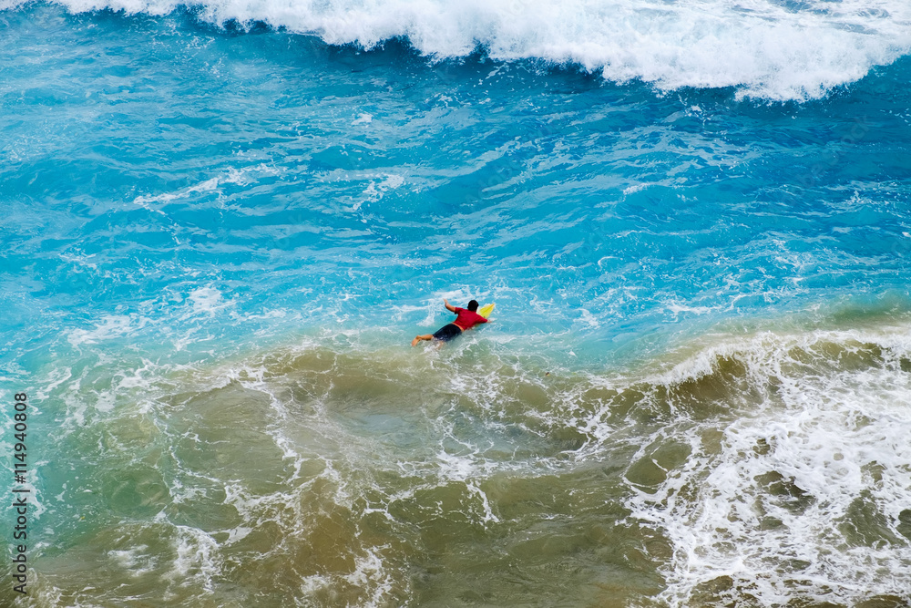 Aerial view of Surfer swimming on a board near huge blue ocean wave in Bali