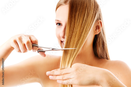 Young blonde woman cutting her hair with scissors.