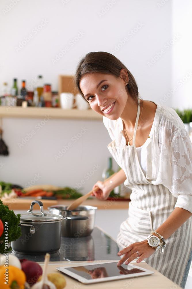 Young woman using a tablet computer to cook in her kitchen . Young woman using a tablet computer to cook in her kitchen .