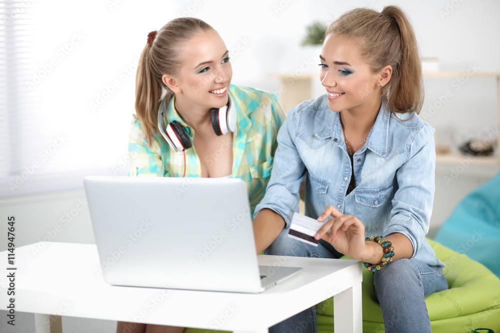 Two young women sitting with laptop and credit cart at home Two young women sitting with laptop and credit cart at home