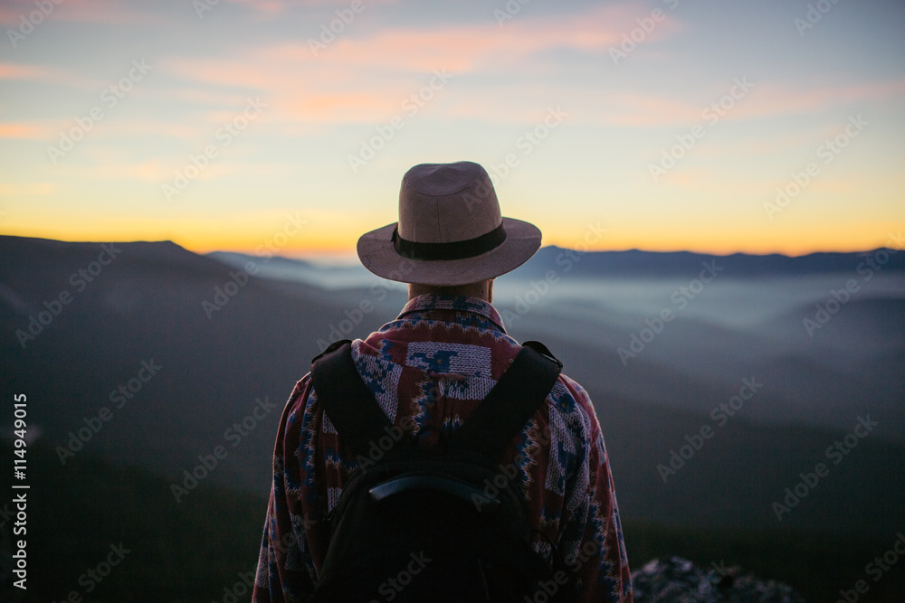 Man with hat and bag looking at the sunset from a mountain