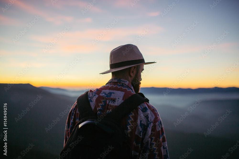 Man with hat and bag looking at the sunset from a mountain Man with hat and bag looking at the sunset from a mountain
