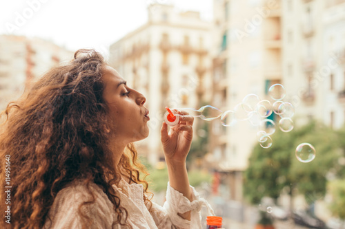   Girl playing with air bubbles. Young woman plays blows an air bubble toy like a little child  having fun on a sunny day outdoors