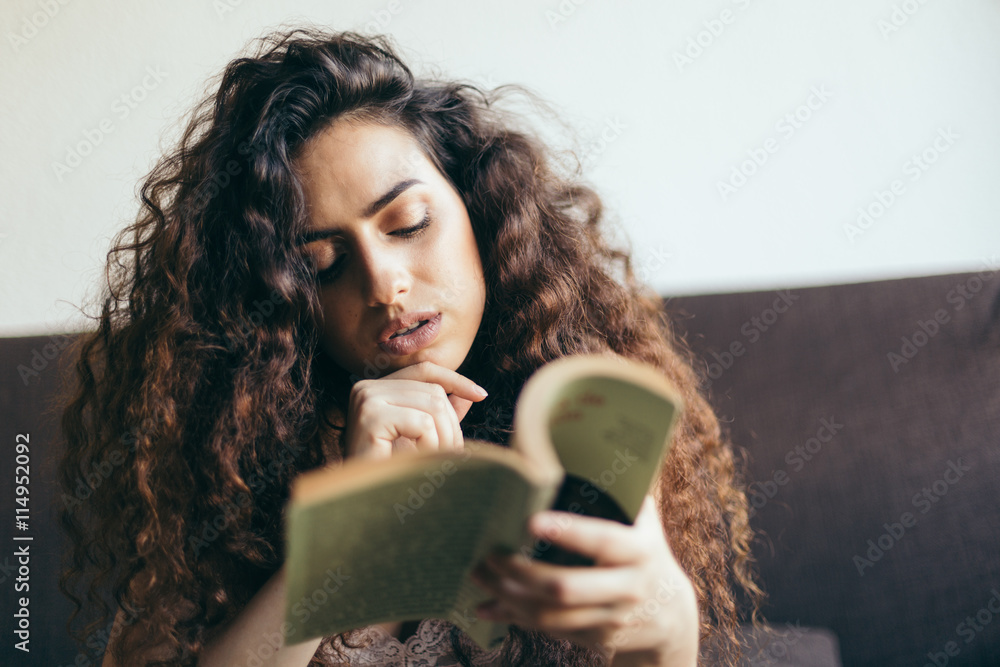 Obraz premium Young girl reading a book on the sofa, with curly hair and fairly dressed