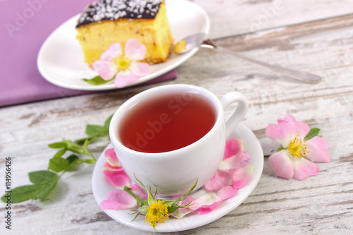 Cup of tea with cheesecake and wild rose flower on old wooden background