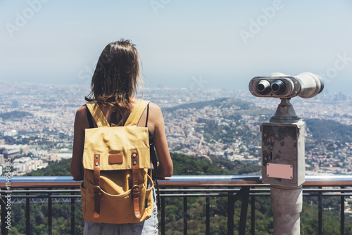 Hipster young girl with bright backpack looking on observation deck, travel plan. Tourist traveler on background panoramic view of the city,  binoculars. Mock up for text message. Barcelona  photo