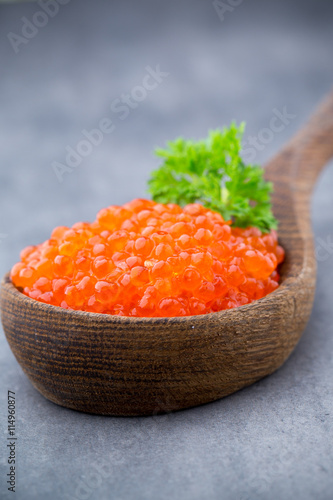 Salmon caviar with spoon on gray background.
