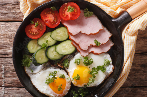 fried eggs with ham, tomatoes and cucumbers close-up. Horizontal top view 