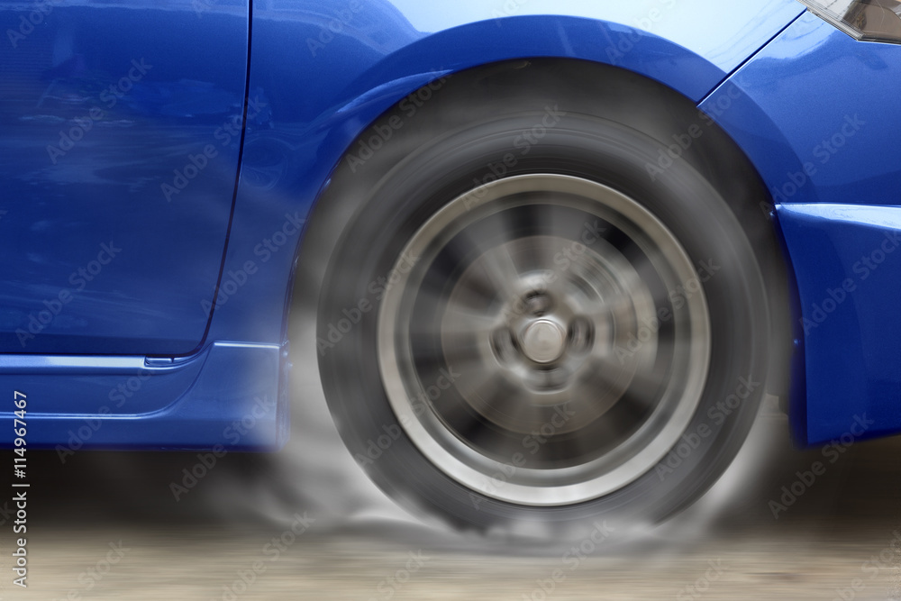 Blue car racing spinning wheel burns rubber on floor.