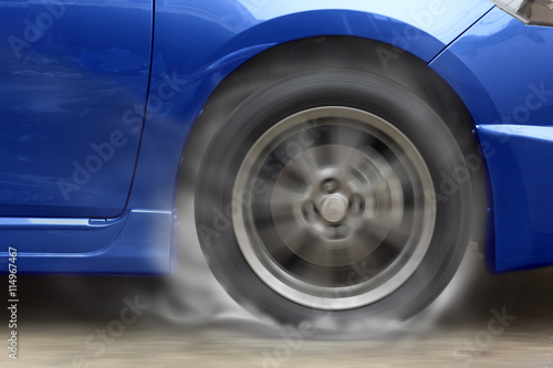 Blue car racing spinning wheel burns rubber on floor. © jayzynism