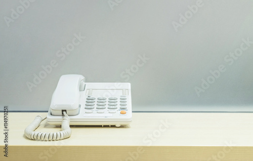 Closeup white phone , office phone on blurred wooden desk and frosted glass wall textured background in room at the office