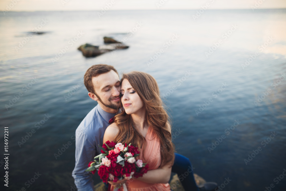 Wedding couple kissing and hugging on rocks near blue sea Wedding couple kissing and hugging on rocks near blue sea