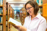 Portrait of a young student reading a book in a library