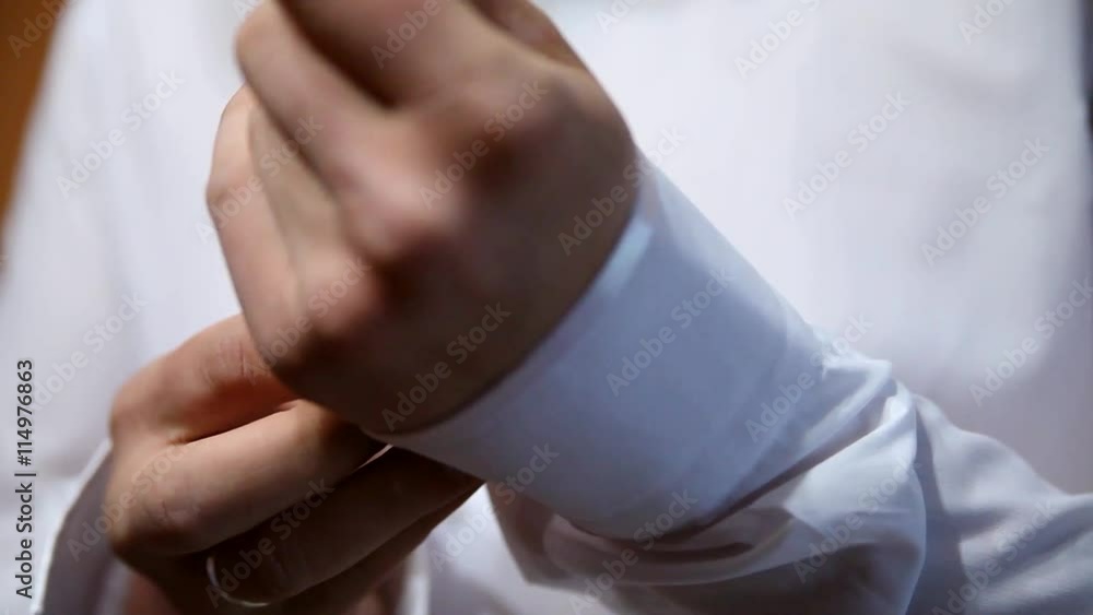 A groom putting on cuff-links as he gets dressed in formal wear .Groom's suit A groom putting on cuff-links as he gets dressed in formal wear .Groom's suit