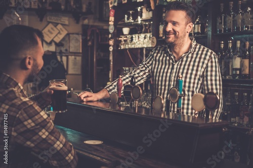 Handsome bartender talking with customer at bar counter in a pub.
