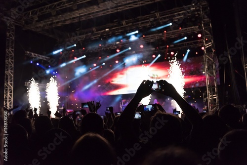 Rock concert, silhouettes of happy people raising up hands in front of bright stage lights. Space in top side.