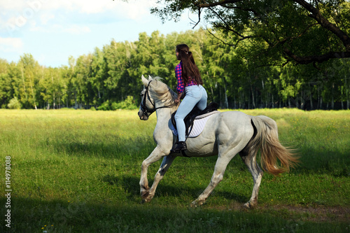Cowgirl riding white horse down the path in the evening park 