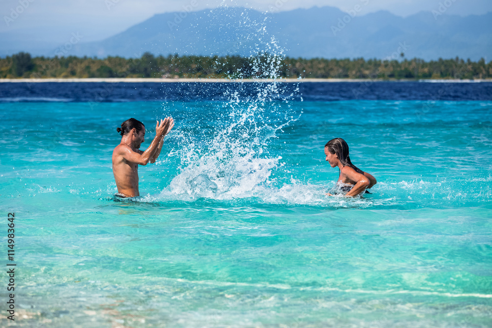 Young couple having fun and splahing the water of a sea
