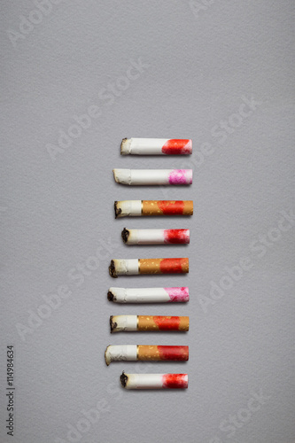 Colored butts / Creative still life of different cigarette stubs with lipstick on grey background.