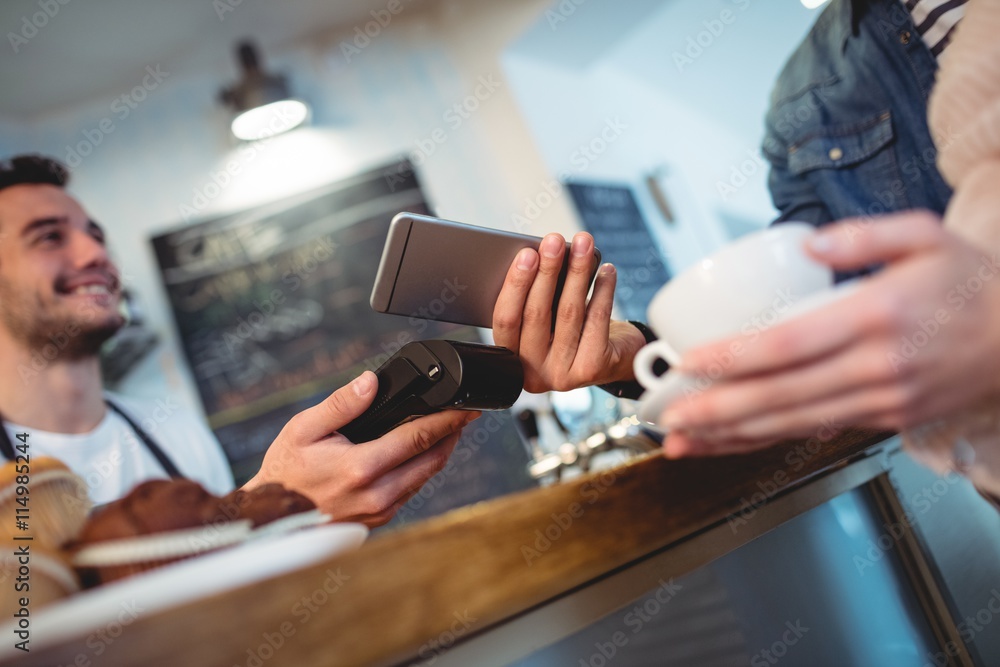 Customer with cellphone standing with barista at cafe Customer with cellphone standing with barista at cafe