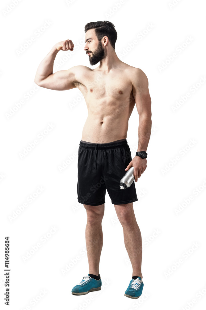 Strong fit young shirtless man flexing bicep muscle and holding water bottle. Full body length portrait isolated over white studio background. Strong fit young shirtless man flexing bicep muscle and holding water bottle. Full body length portrait isolated over white studio background.