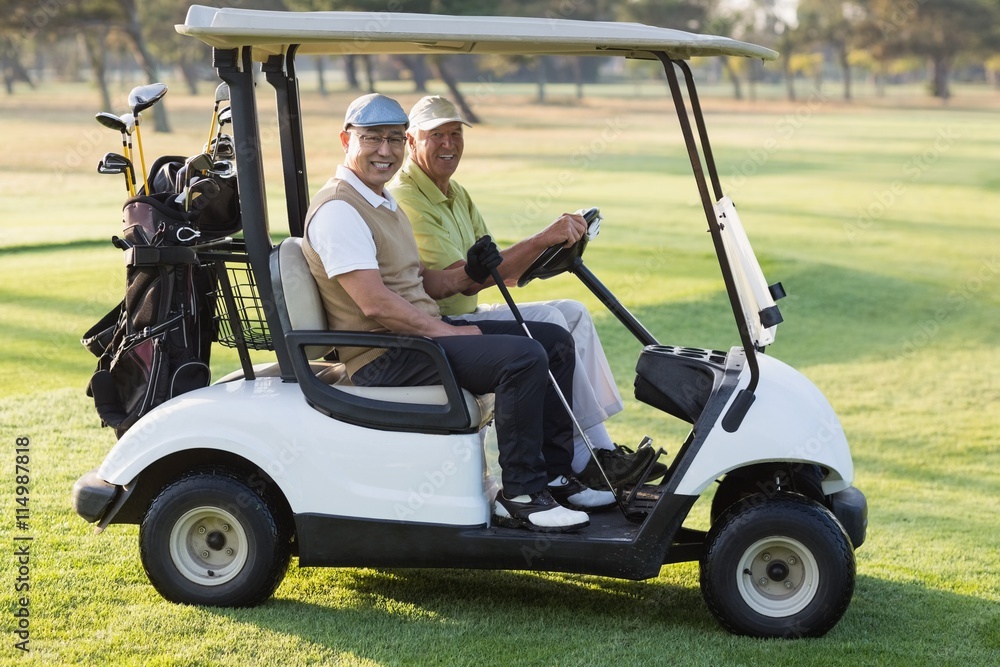 Happy male golfer friends sitting in golf buggy