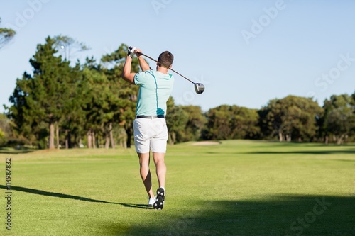 Rear view of young golfer man taking shot 