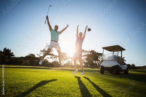 Full length of golf player couple with arms raised 