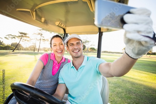 Golfer couple taking selfie while sitting in golf buggy