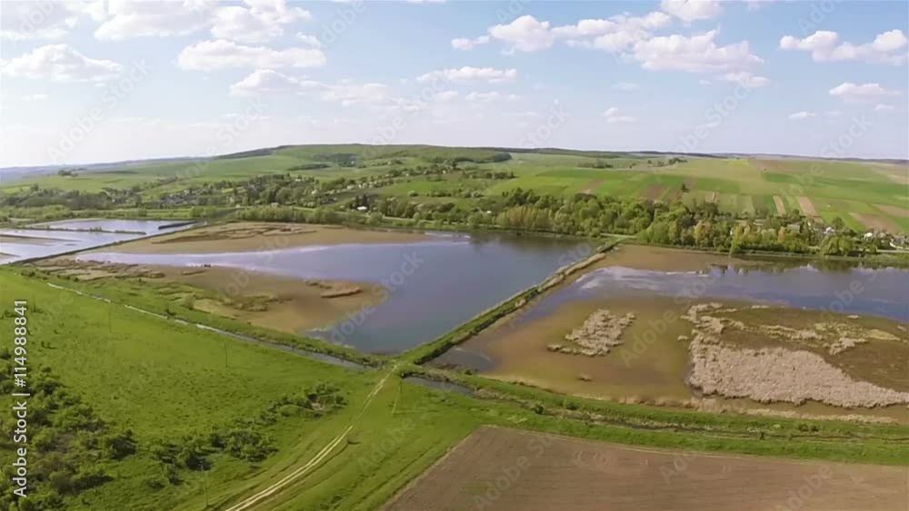 Aerial. Flight over  green field with lakes in distance and blue sky with clouds