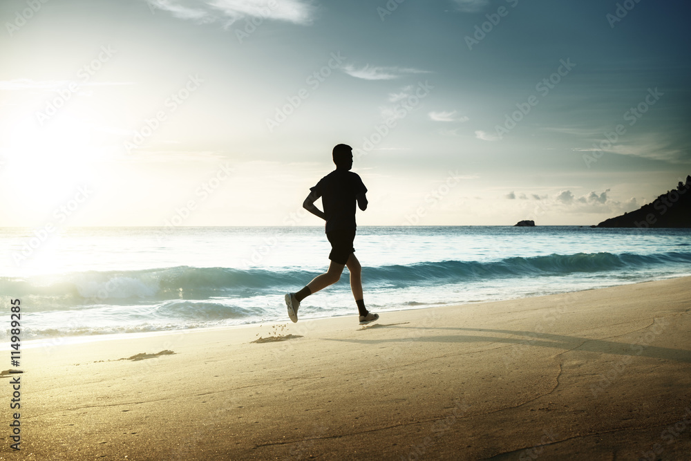 Man running on tropical beach at sunset